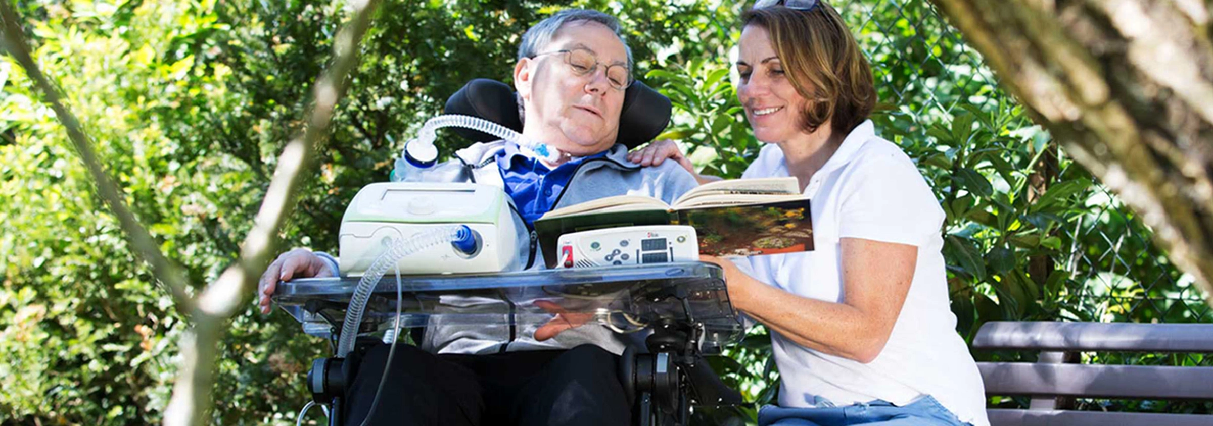 Pflegekraft begleitet einen intensivpflegebedürftigen Mann im Rollstuhl im Freien