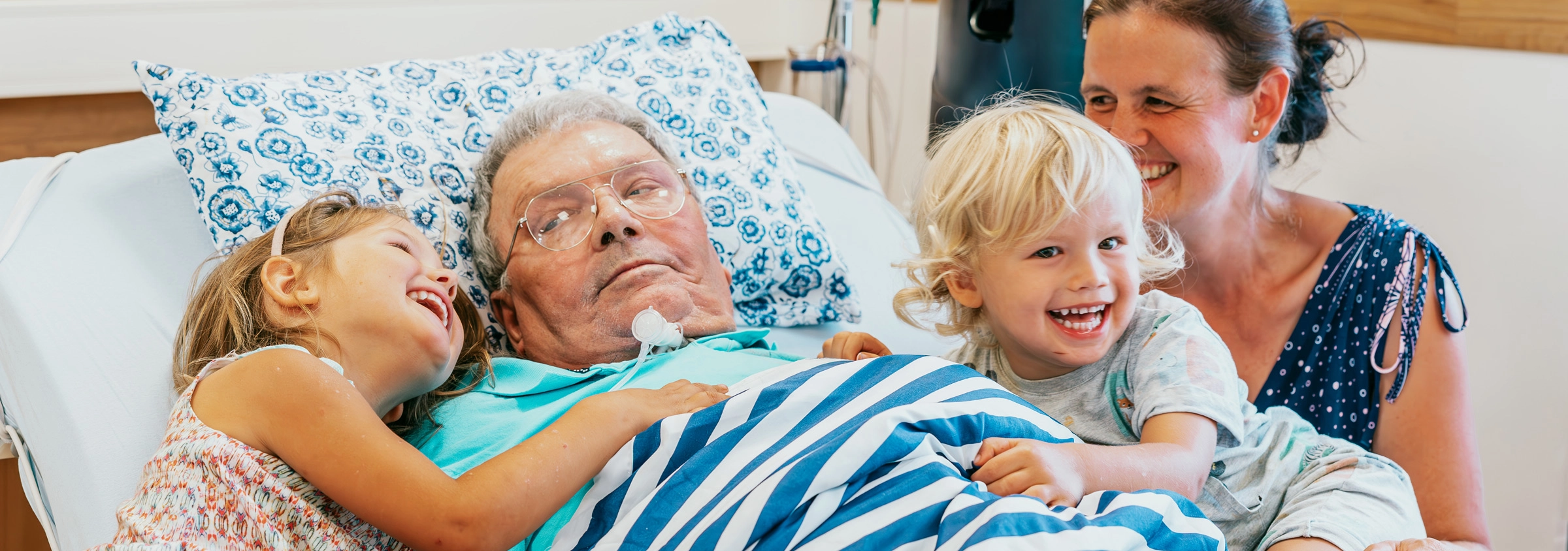 Familie besucht einen pflegebedürftigen Mann im Bett