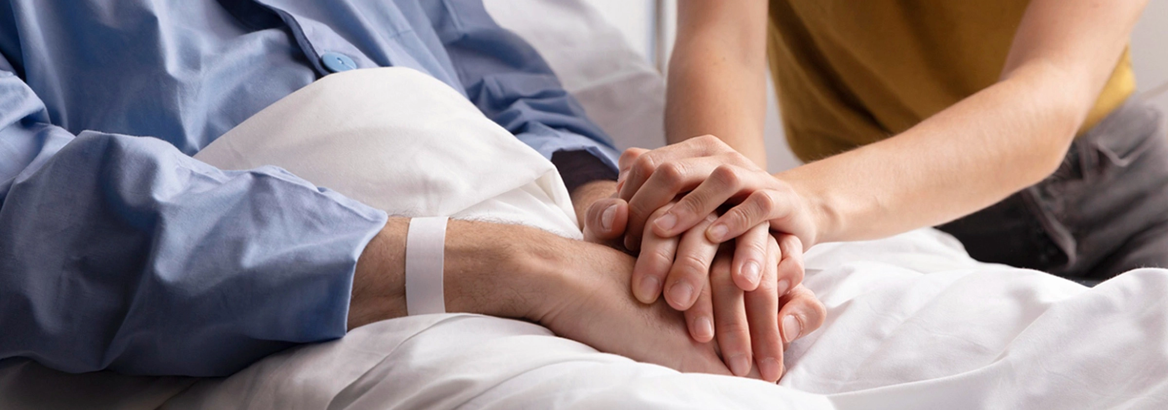 Pflegekraft hält beruhigend die Hand einer Person im Krankenbett