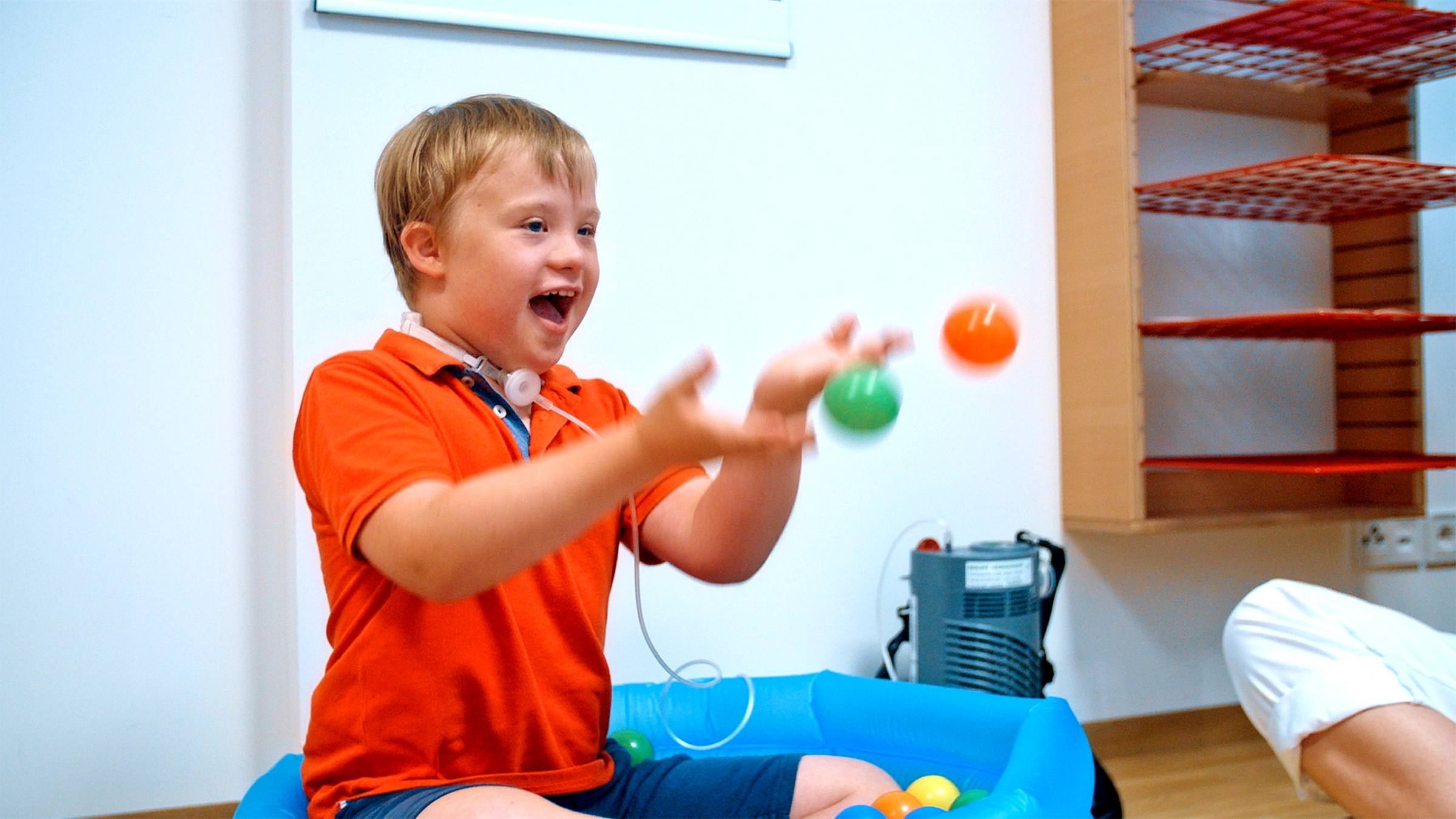 ein Junge mit Trachealkanüle spielt freudestrahlend in einem Bällebad.