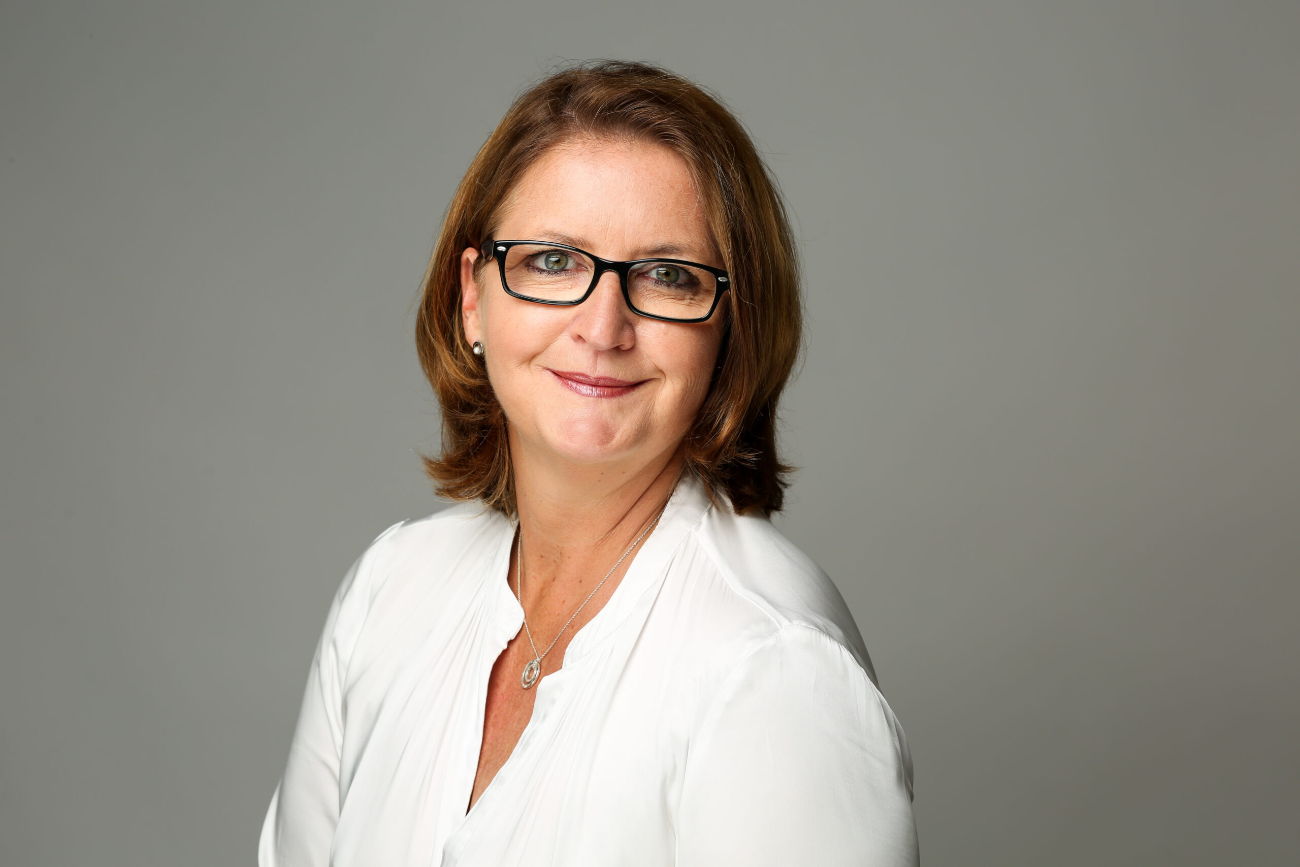Ein Portrait der Case Managerin Michaela Bürger in weißer Bluse vor hellem Hintergrund.