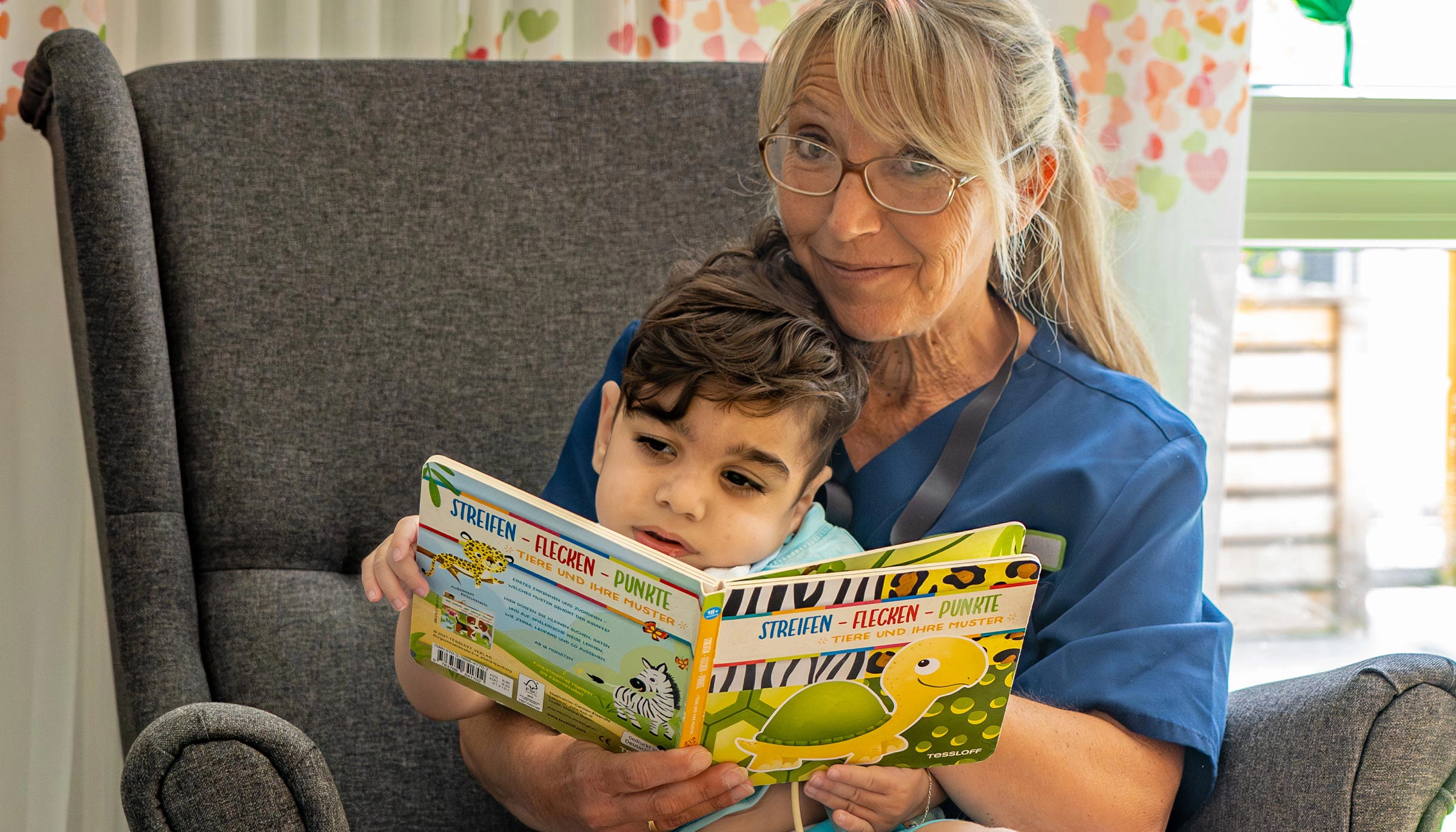 Pflegefachkraft liest gemeinsam mit einem Kind aus einem Bilderbuch
